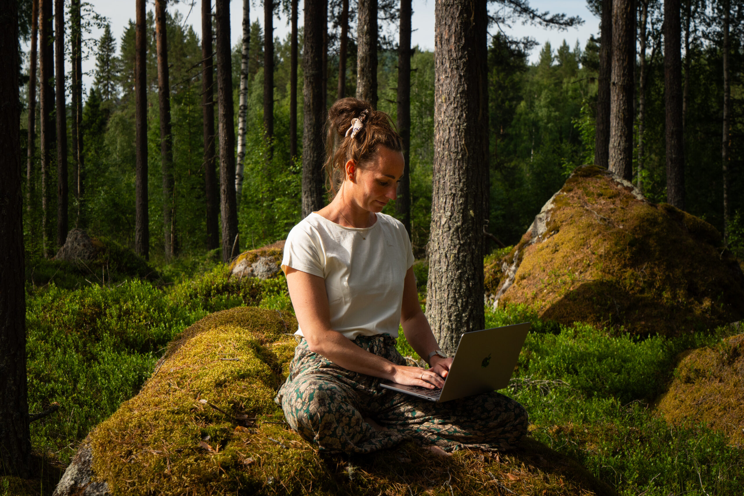 Marielle zittend op een steen met haar laptop in het bos in Zweden