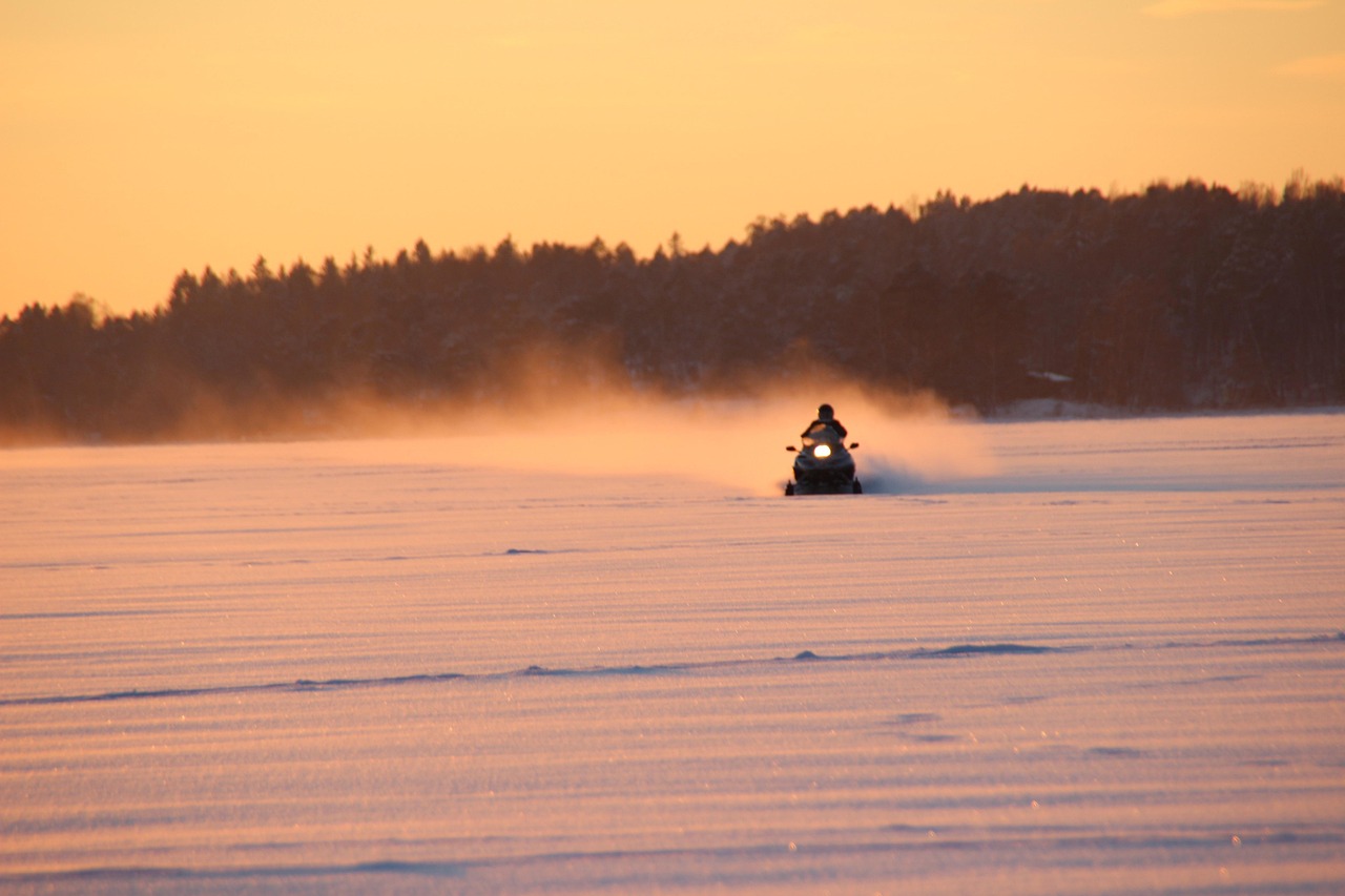 Een sneeuwscooter over het bevroren meer met ondergaande zon bij Friluft Sweden