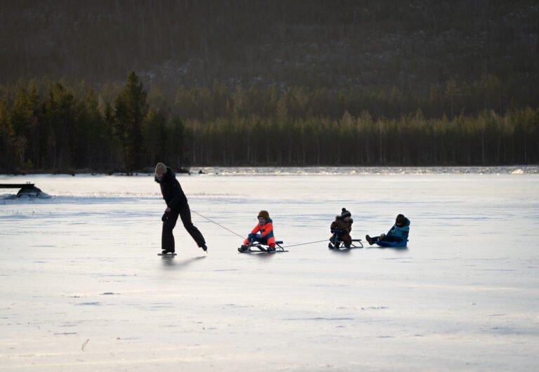 Schaatsen op het bevroren meer meer drie kinderen op een slee erachter tijdens de Winter gezinsweek bij Friluft Sweden